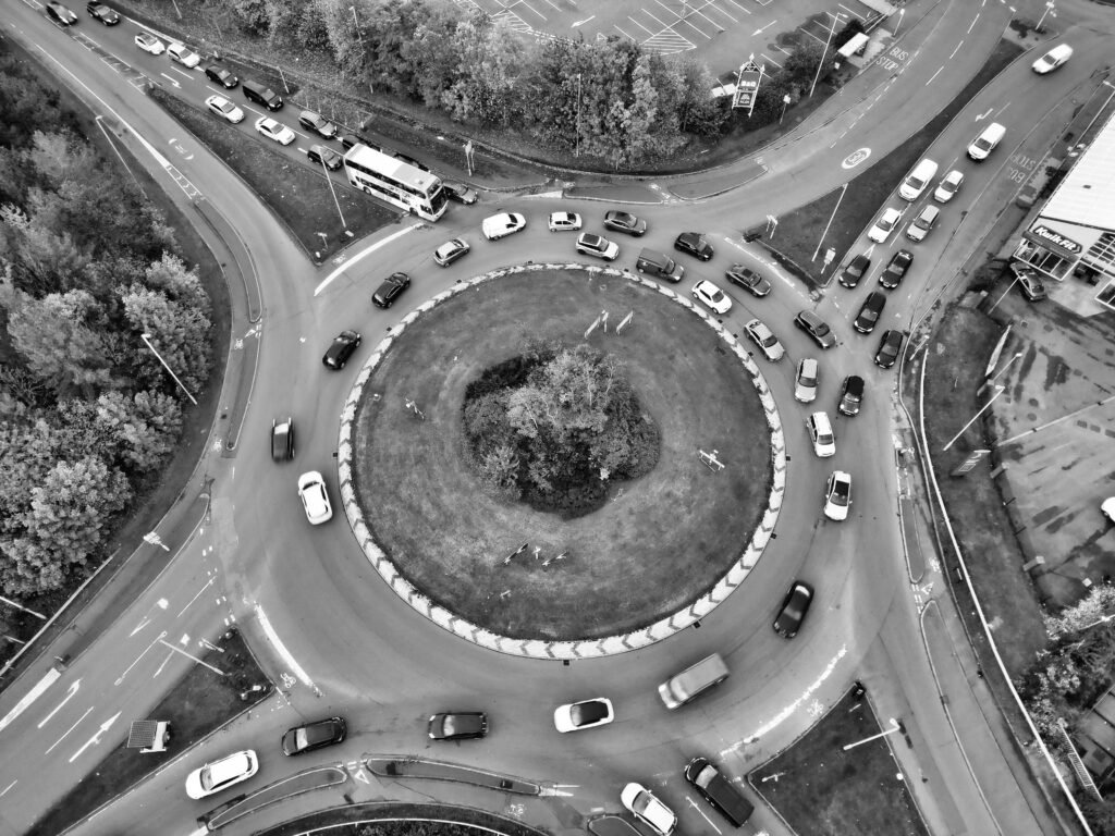 Drone shot of a bustling roundabout in England, capturing cars and greenery, in black and white.